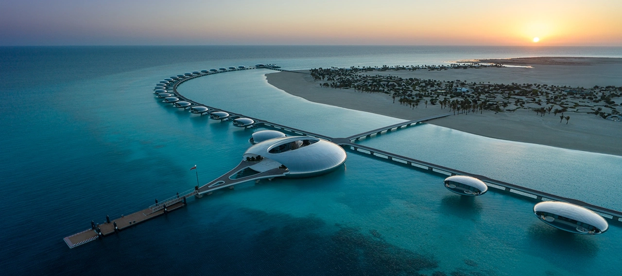Aerial view of Shebara Resort at sunset, featuring a crescent of mirrored overwater villas and a central circular building.